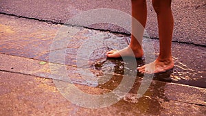 Feet of a barefoot child stand in a puddle during golden hour as gentle raindrops fall