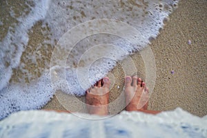 Feet on beach background. Top view on naked feet and legs in sand with wave motion coming to the foot - foaming sea texture.