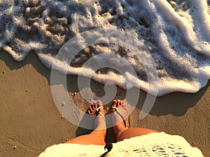 Feet on beach background. Top view on naked feet and legs in sand with wave motion coming to the foot - foaming sea texture.