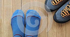 Feet with blue hiking socks move toes, next to trekking shoes, on wooden floor