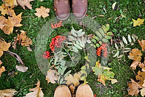 Feet in boots with rowanberries and autumn leaves