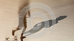 feet of boy running along the beach in the water with shadow and reflection in water