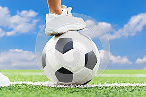 Feet of a boy wearing white sneakers stepping on a soccer ball