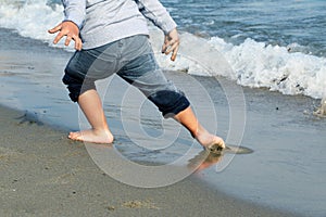 Feet of the boy in wet gray jeans escaping from the wave on sandy beach