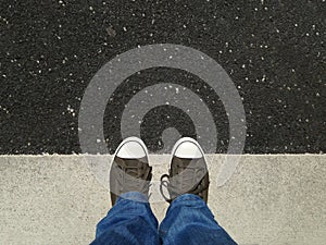 Feet in canvas shoes standing on asphalt aligned with road markings