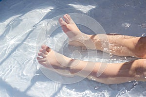 Feet of a child in the blue water of a children`s pool. Fun summer outdoor activities, swimming and enjoying the water.