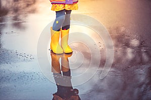 Feet of child in colorful  rubber boots jumping over puddle in rain. Autumn park