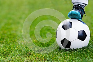 Feet of child on football / soccer ball on grass.