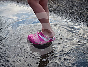 Feet of child in pink shoes standing in a puddle in the rain