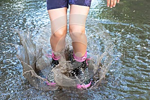 Feet of child in rubber boots jumping over a puddle and water splashes