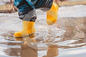 Feet of a child in rubber boots stomp through puddles