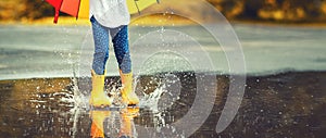 Feet of child in yellow rubber boots jumping over puddle in ra