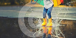 Feet of child in yellow rubber boots jumping over puddle in ra