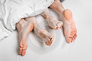 Feet of a couple in bed under the blanket