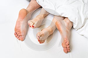 Feet of a couple in bed under the blanket