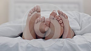 Feet, couple and rubbing in bedroom in home, relax in peace or rest in blanket in the morning together. Barefoot, bed