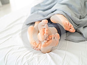 Feet of couple sleeping side by side in comfortable bed. Close up of feet in a bed under white blanket. Bare feet of a