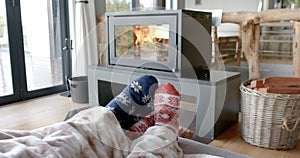 Feet of couple on sofa in warm socks under blanket in front of fireplace at home, in slow motion