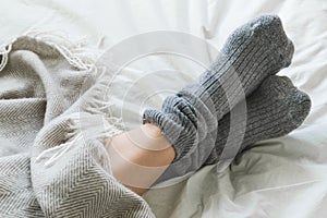 Feet crossed with gray socks on bed under blanket