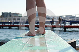 feet of a diver ready to dive off a blue diving board pocking out over the waves in a bay and protected sea bath in Geelong,