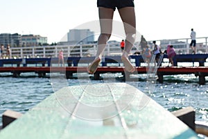 feet of a diver ready to dive off a blue diving board pocking out over the waves in a bay and protected sea bath in Geelong,