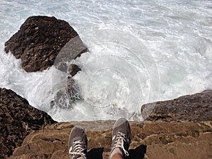 Feet on the edge of rock on the Ocean with foamed waves