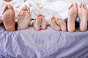 Feet of family lying in bed. Closeup of feet of parents and children in bed. Family relaxing in bed together. Below bare