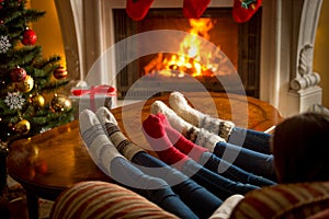 Feet of family in woolen socks warming at burning fireplace at l