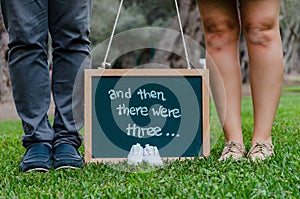 Feet of father and mother with baby shoes and a black slate