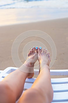 Feet of a girl on a deck-chair meeting sunrise-sun, sea, beach