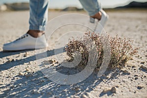 The feet of a girl in white sneakers are walking in a desert area