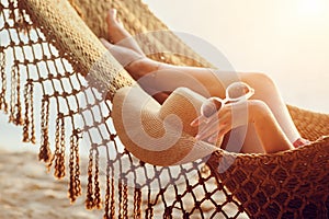 Feet and hand relaxing woman in hammock on the beach during sunset.