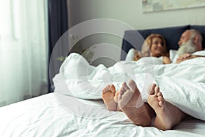 Feet of happy mature couple resting together in bed