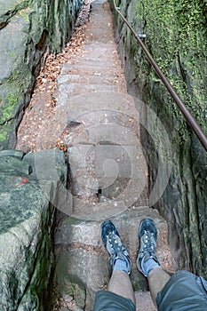 Feet in hiking boots of a male explorer standing on top of a staircase between narrow rocky groove