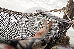 Feet and legs of a girl lying on net hammock bed by the sea