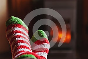 Feet legs in winter clothes wool socks at fireplace at home on winter or autumn evening relaxing and warming up