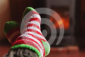 Feet legs in winter clothes wool socks at fireplace at home on winter or autumn evening relaxing and warming up