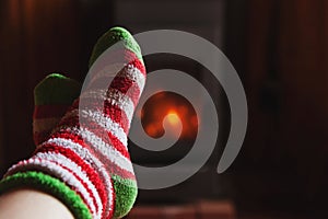 Feet legs in winter clothes wool socks at fireplace at home on winter or autumn evening relaxing and warming up