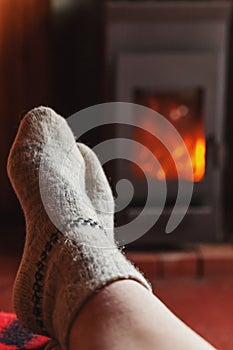 Feet legs in winter clothes wool socks at fireplace at home on winter or autumn evening relaxing and warming up