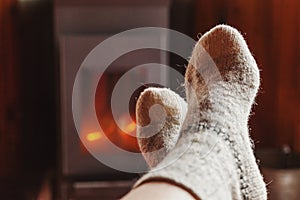 Feet legs in winter clothes wool socks at fireplace at home on winter or autumn evening relaxing and warming up