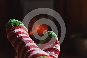 Feet legs in winter clothes wool socks at fireplace at home on winter or autumn evening relaxing and warming up