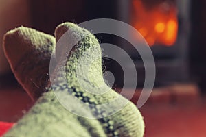 Feet legs in winter clothes wool socks at fireplace at home on winter or autumn evening relaxing and warming up