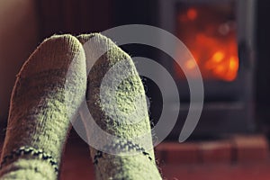 Feet legs in winter clothes wool socks at fireplace at home on winter or autumn evening relaxing and warming up