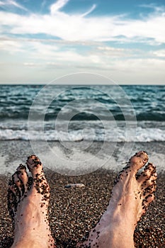 The feet of a lying man on a sandy beach near sea