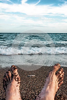 The feet of a lying man on a sandy beach near sea
