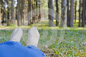 feet lying resting on grass in pine tree forest. leg wearing jeans relaxing in park