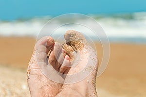 Feet of a man lying on the beach. Vacationer relaxes near the azure sea at sunny day.