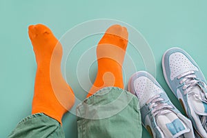 The feet of a man in orange socks with his sneakers take off. Mint green background.