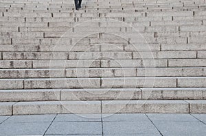 Feet of a man stepping up grey concrete stone stairs upwards