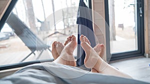 The feet of a married couple sticking out from under the blanket in a country house with panoramic windows.